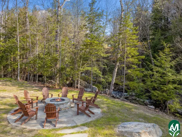 Eight outdoor chairs around a fire pit near the woods. This is for the blog post titled Fire Pit Ideas, Tips for Installation, and Costs.