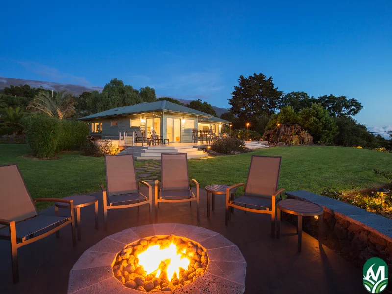 3 chairs around a fire pit with a modern house in the background. This image is for the service page titled Fire Pit Installation.