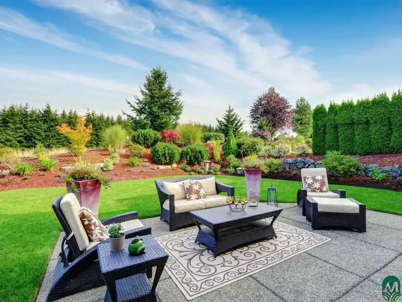 Backyard with manicured shrubs and trees, outdoor furniture, and a patio by way of a professional patio installation service